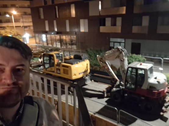 Selfie nocturne sur fond de deux deux tractopelles, une jeune (à gauche), une blanche (à droite).