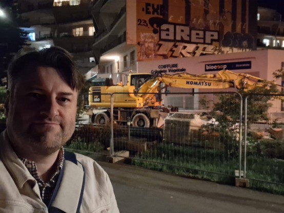 Selfie nocturne sur fond de tractopelle jaune derrière une barrière