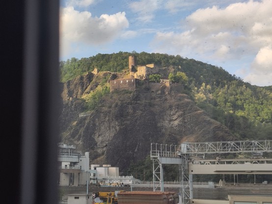 colline surmontée d'un château avec une usine en contrebas vue de la fenêtre d'un train.